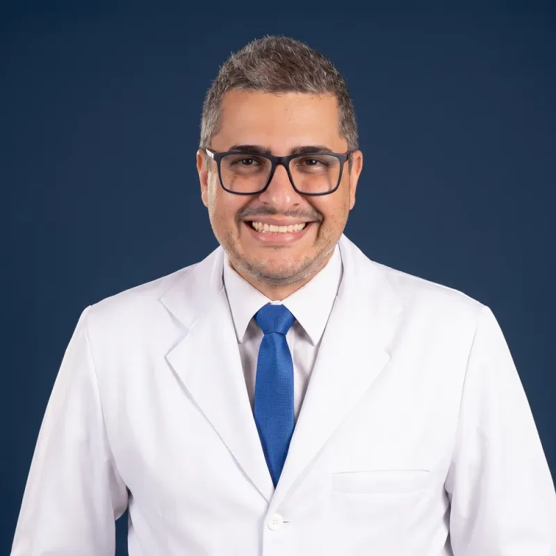 Conrado Augusto sorrindo com jaleco e óculos